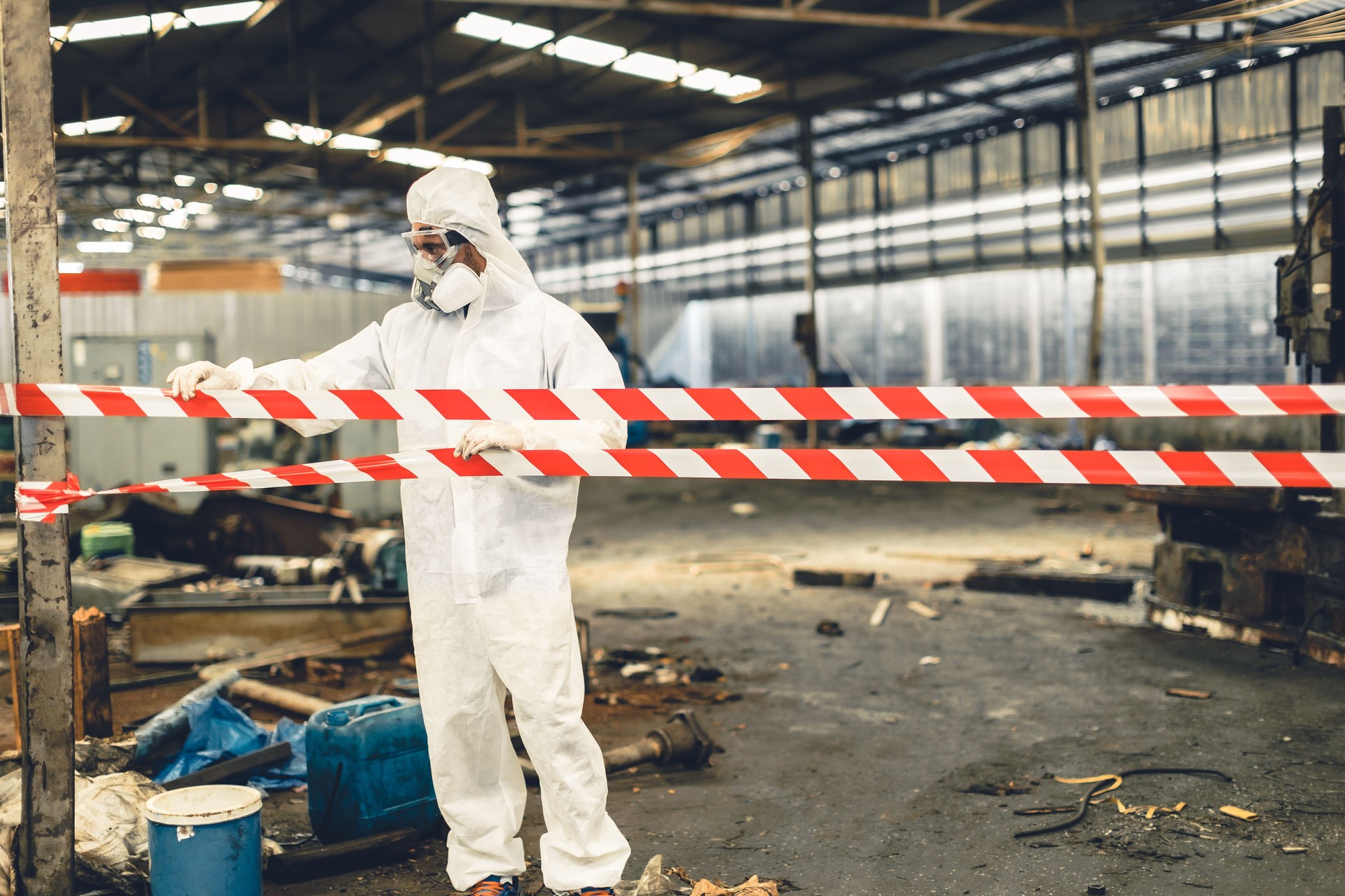 Worker in PPE safety suit with area closed barricade security tape in danger dirty area from virus infected chemical leak