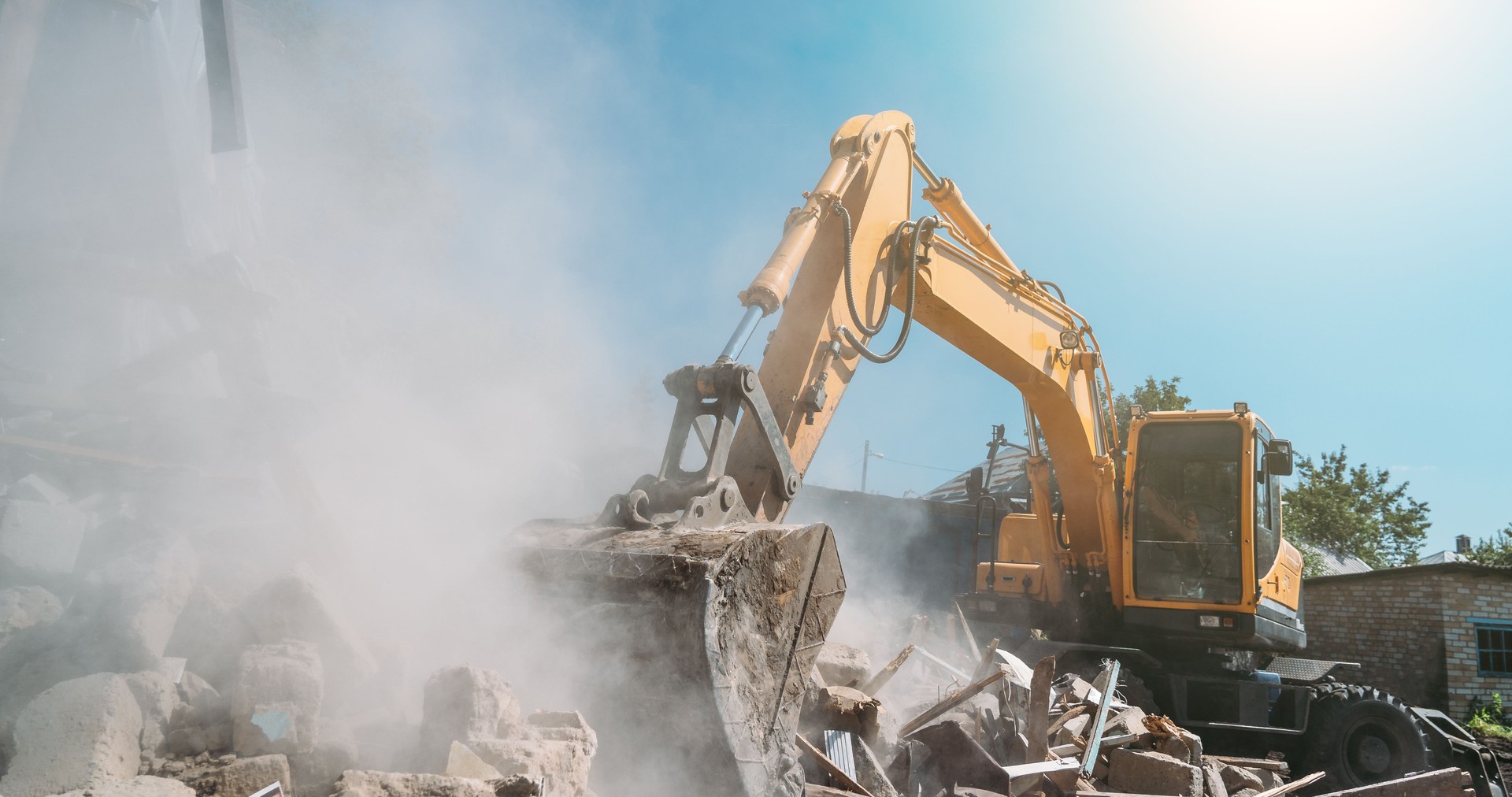 Destruction of old house by excavator. Bucket of excavator breaks concrete structure